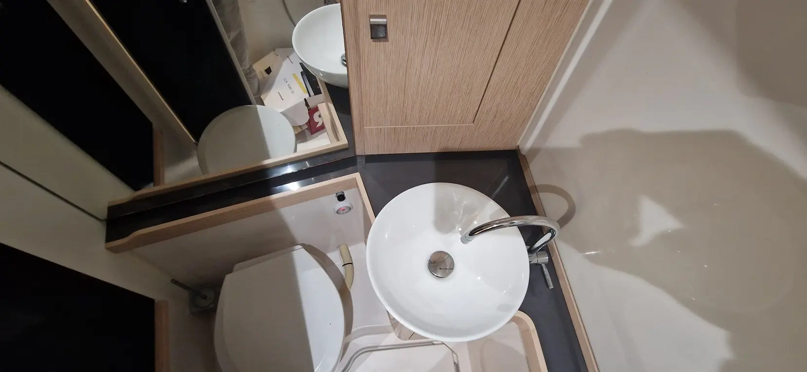 Modern bathroom featuring a white sink, toilet, and wooden cabinetry with a mirror reflecting the surroundings.